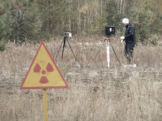 Messung der Radioaktivität in der Sperrzone rund um das havarierte Kernkraftwerk Tschornobyl mit zwei verschiedenen Typen von Gammaspektrometern – im Vordergrund warnt ein Schild vor erhöhter Radioaktivität (Bild anzeigen)