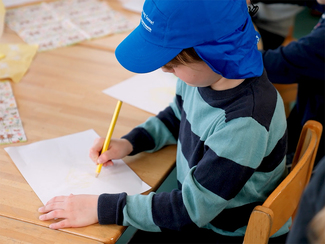 Junge mit einer Sonnenschutzschirmmütze malt mit einem Buntstift auf Papier (Bild anzeigen)