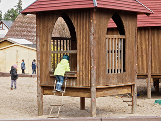 Kind klettert über eine Hängeleiter in ein Holzhaus (Bild anzeigen)